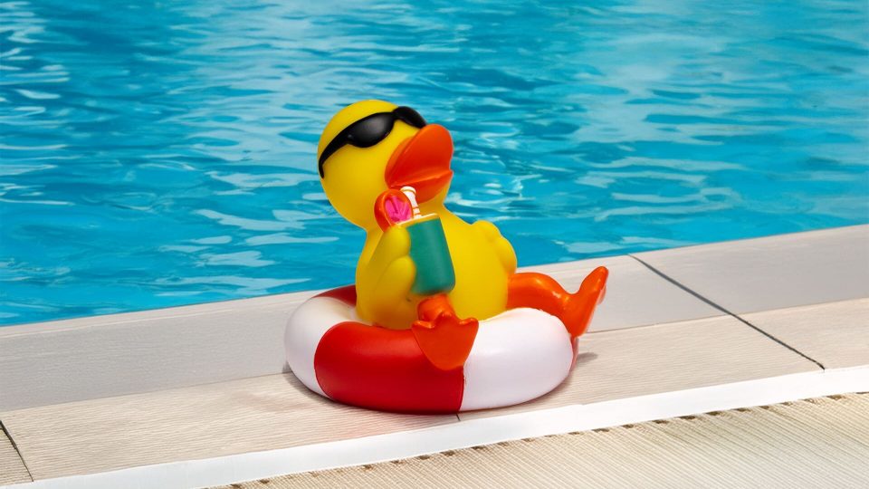Gummiente im Schwimmring mit Cocktail – bearbeitet am Poolrand mit Pool im Hintergrund